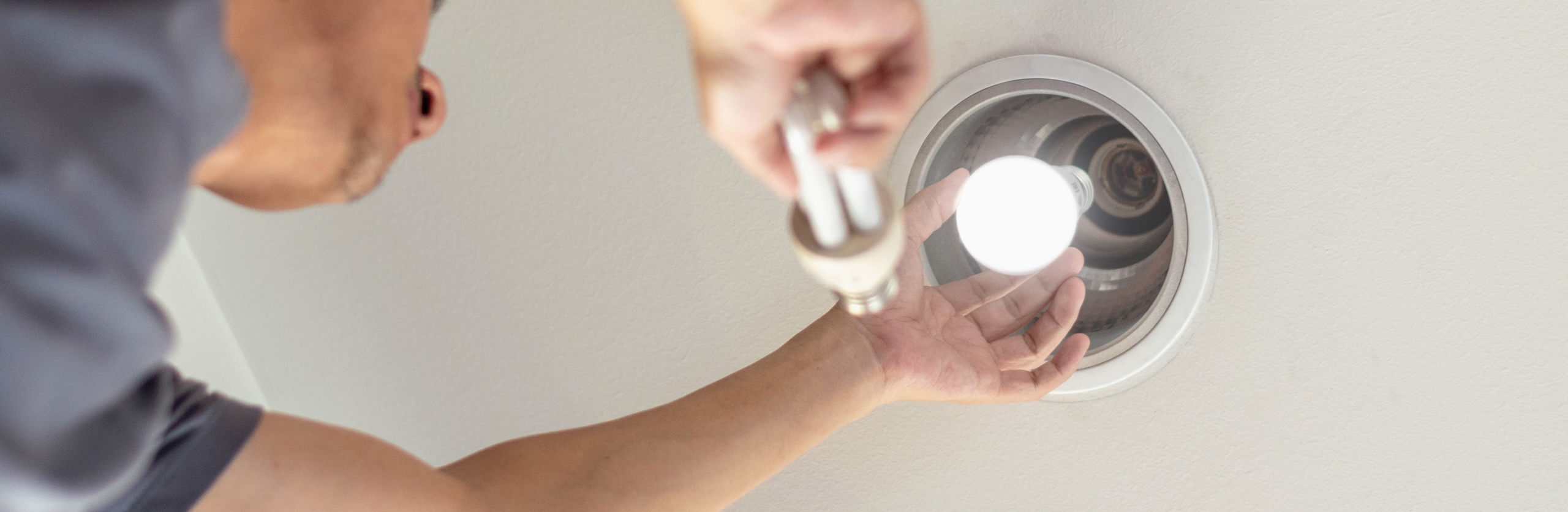 Power saving concept. Hands holding new Light Emitting Diode ( LED ) light bulb with light on and blur spiral compact-fluorescent (CFL) bulbs behind for copyspace.
