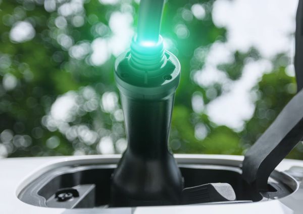 EV charger plug into electric car for electric recharge by electric charging station with glowing light cable, below tree closeup. Cutting-Edge innovation of green future energy sustainability Peruse