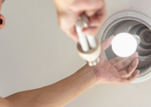 Power saving concept. Hands holding new Light Emitting Diode ( LED ) light bulb with light on and blur spiral compact-fluorescent (CFL) bulbs behind for copyspace.